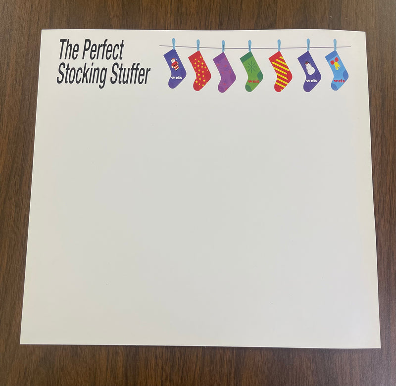 A white card stock sign topper with the text 'The Perfect Stocking Stuffer' and a graphic of socks hanging from a rod, designed to be placed on top of a sign frame or holder.