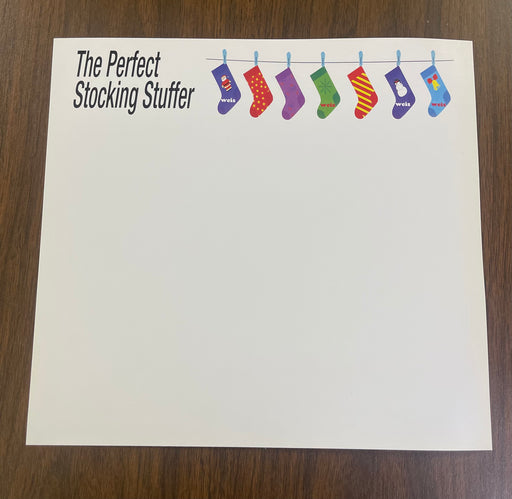 A white card stock sign topper with the text 'The Perfect Stocking Stuffer' and a graphic of socks hanging from a rod, designed to be placed on top of a sign frame or holder.