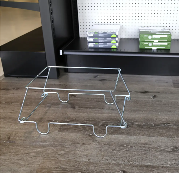 A silver metal wire display stand or shelf insert placed on a wood-look floor in front of black shelving with storage boxes on a pegboard wall.