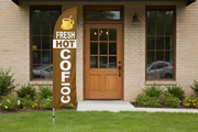 Brown and cream Coffee feather flag planted in landscaped grass outside a café, 11.5'H x 2.5'W outdoor promotional sign with aluminum pole and ground spike