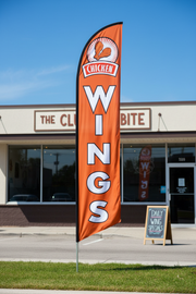 Orange Chicken Wings feather flag planted in grass outside a restaurant – 16' tall outdoor display – Screen Gems Inc.