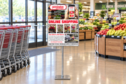 Custom 22 × 28 Pennington online-shopping poster in a chrome floor stand beside carts at a supermarket entrance.