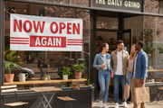 Now Open Again vinyl banner hung on the exterior window or entrance of a retail store or restaurant reopening, welcoming community atmosphere with customers approaching the entrance in bright natural daylight
