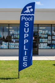Blue Pool Supplies feather flag planted in grass in front of a pool supply store – 16' tall outdoor display – Screen Gems Inc.