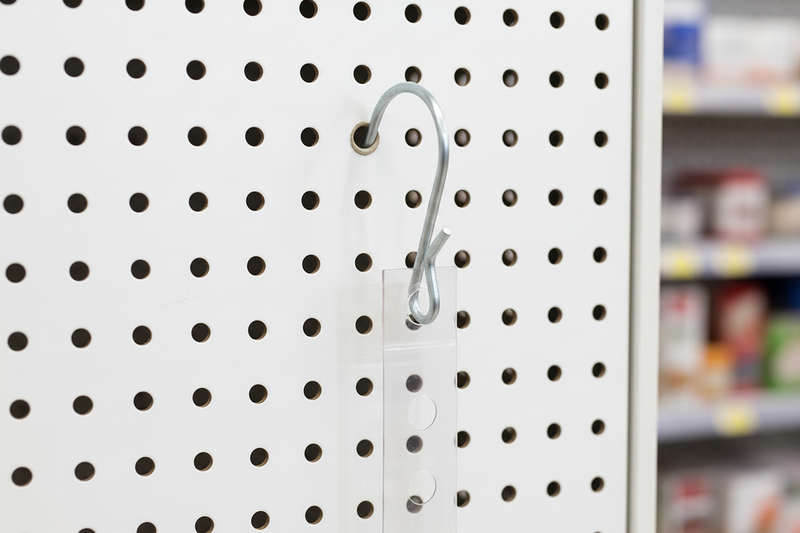 Close-up of a galvanized pinched S-hook inserted through a round perforated gondola shelf hole and attached to a clear merchandising strip