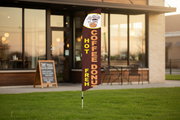 Coffee and Donuts feather flag kit displayed outdoors in grass in front of a cafe storefront, 11.5ft flag on aluminum pole with ground spike
