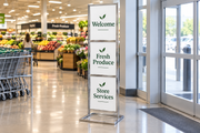 Chrome triple-tier 22 × 28 floor sign stand with an open rectangular base displaying three messages at a supermarket.