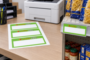 Weekly Valu green three-up laser-compatible shelf sign sheet beside printer with one sign in a grocery shelf holder
