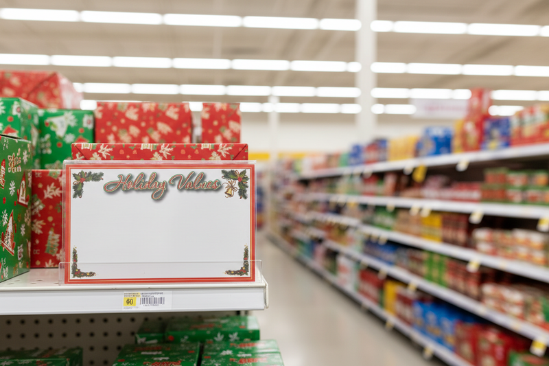 Festive Holiday Values shelf sign with holly and bell design in clear sign holder on retail store shelf – lifestyle holiday in-store display