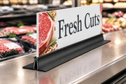 24-inch black sign foot holder with a wide stabilizing base supporting an illustrative Fresh Cuts sign in a supermarket; sign sold separately