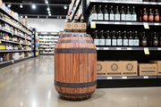 Custom printed 3-foot barrel display standee positioned beside beer and wine shelves in a beverage store, lifestyle merchandising view