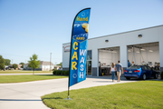 Hand Car Wash feather flag installed in green grass beside an automotive wash bay, showing the outdoor roadside advertising use case