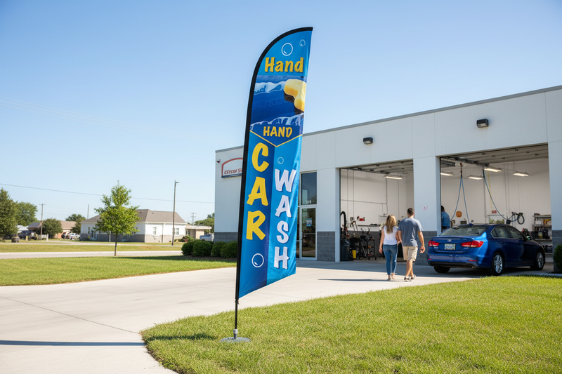 Hand Car Wash feather flag installed in green grass beside an automotive wash bay, showing the outdoor roadside advertising use case