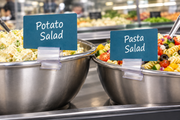 Clear plastic 2-way sign holders saddled on stainless steel deli bowl rims, holding Potato Salad and Pasta Salad signs in a supermarket service case