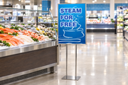 Blue Steam for Free 22 by 28 inch poster in a chrome floor stand beside a supermarket seafood counter; stand sold separately.