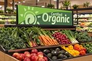 Green vinyl organic produce category header displayed above a supermarket produce island with carrots and leafy greens