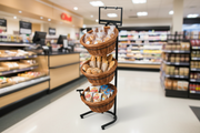 Full-height three-tier black steel floor display fixture with three removable round wicker baskets filled with bakery products in a grocery store