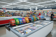 Refrigerated coffin case adjustable bridge rack installed on top of a grocery store coffin cooler with cross-merchandised snacks and beverages on display.