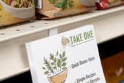 Translucent natural beige arrowhead coupon dart holding a take-one pad on a grocery shelf price channel.