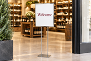 Chrome 22 × 28 bulletin sign holder with two support posts and flat base displaying a welcome poster in a wine store.