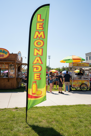 Green Lemonade feather flag planted in grass at an outdoor concession or food vendor location – 16' tall display – Screen Gems Inc.
