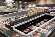 Black steel bunker case cross-merchandising rack displaying seasoning packets above packaged meat in a supermarket case