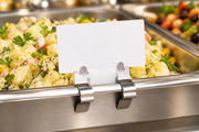 Stainless steel deli pan sign clip holding a blank food label on a deli tray in a supermarket food case