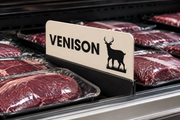 Illustrative venison game meat case divider in a holder among packaged meat in a supermarket display