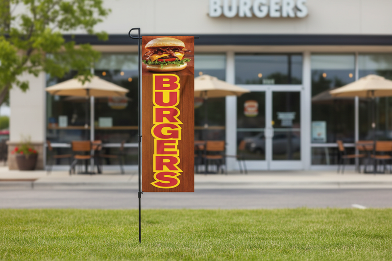 Burgers banner flag kit using the original burger artwork, planted in landscaped grass outside a burger restaurant with the full pole and ground spike visible
