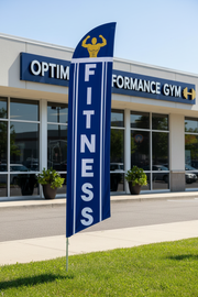 Blue and gold Fitness feather flag planted in grass outside a gym or fitness center – 16' tall outdoor display – Screen Gems Inc.