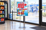 Touch Free Car Wash 22 × 28-inch poster with red lettering and cartoon car displayed in a floor stand near a convenience store entrance.