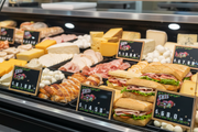 Deli dial-a-price tags displayed beside sliced meats, cheeses, prepared foods, and sandwiches