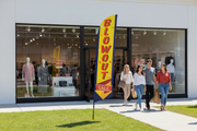 Blowout Sale feather flag installed in green grass outside a retail storefront with shoppers, showing the outdoor sale promotion use case