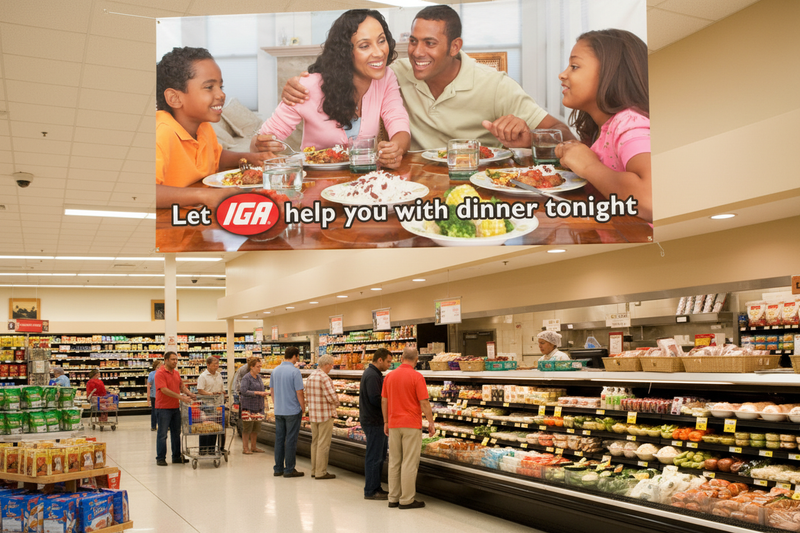 IGA Help with Dinner vinyl banner Design B hung above a deli section inside an IGA supermarket with shoppers browsing prepared foods