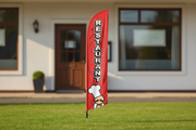 Red Restaurant feather flag with chef artwork planted in green grass outside a restaurant entrance, showing the full pole and ground spike