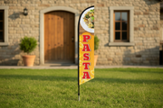Pasta feather flag using the uploaded artwork, planted in grass outside a restaurant entrance with the pointed ground spike visible