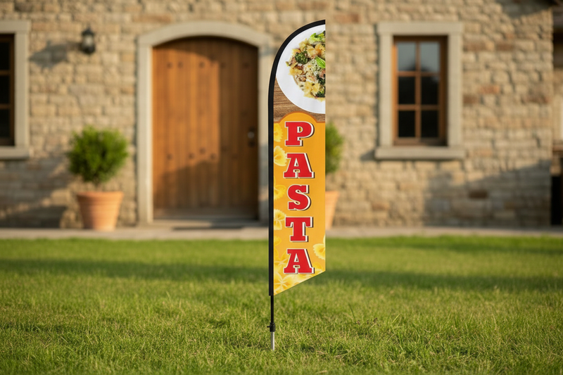 Pasta feather flag using the uploaded artwork, planted in grass outside a restaurant entrance with the pointed ground spike visible