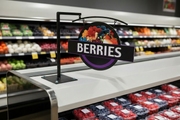 Full-size berries produce sign mounted on the top of a supermarket produce case with visible holder hardware