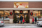 IGA Season's Greetings holiday vinyl banner hung on an IGA supermarket storefront during the holiday season with festive decorations and families shopping