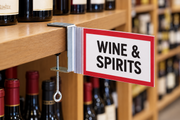 C-clamp aisle invader sign holder displaying a Wine & Spirits sign on a wooden shelf in a wine store.