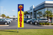 Easy Finance banner flag kit displayed outdoors in grass in front of a car dealership, 12ft rectangular flag on pole with ground spike