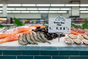 Seafood dial price tag with fish graphic displayed on a fresh seafood counter with salmon, shrimp, mussels, and oysters, lifestyle merchandising view