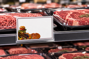 Meat shelf sign with burgundy border and food artwork displayed in a clear holder beside packaged meats.