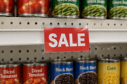 Clear center-mount slim sign protector displaying a Sale card above and below a grocery shelf edge.