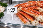 Small white write-on wipe-off case spear pick labeled Crab Legs with pointed stem planted in crushed ice beside a chilled crab leg seafood display