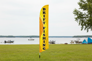 Yellow Drift Fishing feather flag with complete lettering on an aluminum pole and ground spike beside a lakeside campground
